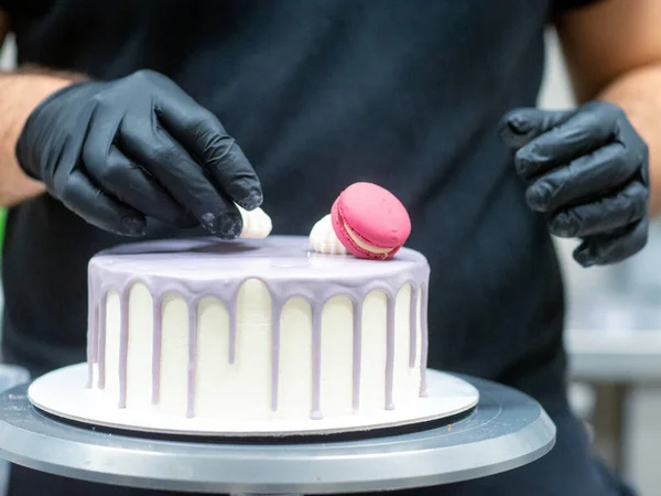 frosted drip cake on stand while designer works on topping