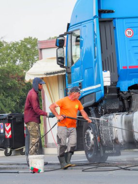 Adam, oto yıkamacıdaki self servis ekipmanlarını kullanarak mavi kamyonun dışını spreyliyor..