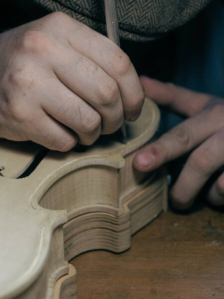 Close up of professional master artisan luthier painstaking detailed work on wood violin in a workshop.