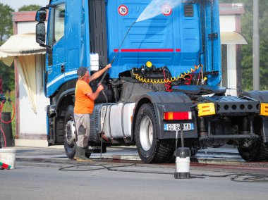 Adam, oto yıkamacıdaki self servis ekipmanlarını kullanarak mavi kamyonun dışını spreyliyor..