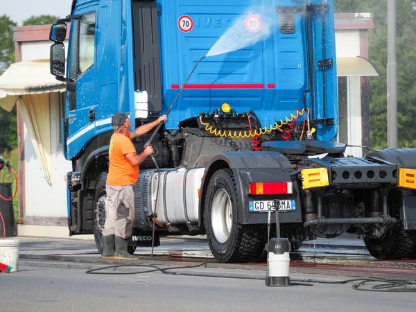 Adam, oto yıkamacıdaki self servis ekipmanlarını kullanarak mavi kamyonun dışını spreyliyor..