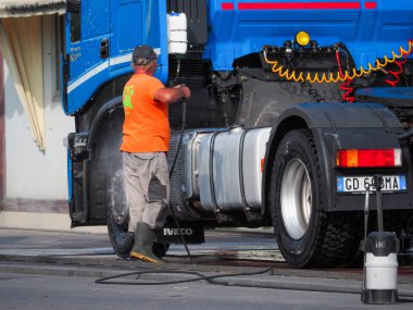 Adam, oto yıkamacıdaki self servis ekipmanlarını kullanarak mavi kamyonun dışını spreyliyor..