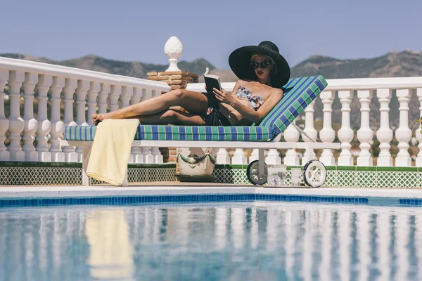 Chica rubia relajante lectura junto a la piscina —  Fotos de Stock