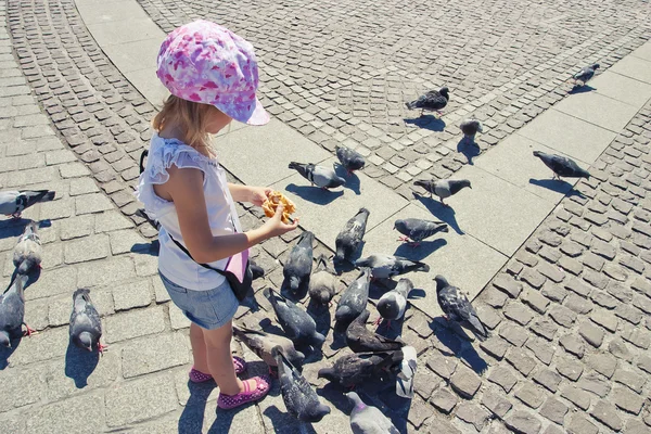 Little girl feeding pigeons on the square — Stock Photo, Image