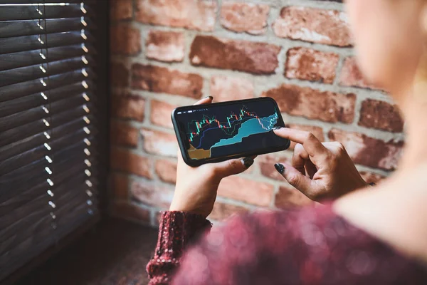 Akıllı telefondaki yatırım uygulamasını kullanarak hisse senedi kripto piyasasına yatırım yapan kişi. Elinde borsa yatırımı var. Cep telefonu tutan tüccar mum grafiğine bakıyor