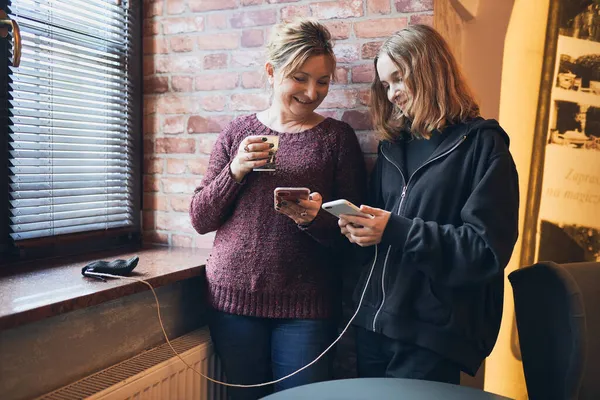 Улыбающиеся Женщины Помощью Смартфонов Пьют Кофе Зарядки Мобильного Телефона Расслабляясь — стоковое фото