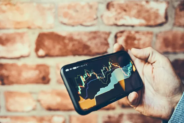 利用智能手机上的投资应用程序在股票加密货币市场上进行交易的人 股市投资在手 拿着手机看蜡烛图的商人 — 图库照片