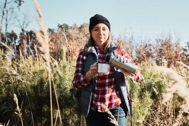 Bir kadın yaz gezisi sırasında dinleniyor ve bir fincan kahveyle dinleniyor. Bir kadın patikada dikiliyor ve başka tarafa bakıyor. Sırt çantalı bir kadın dağlarda uzun otların arasında yürüyüş yapıyor. Yaz tatilini doğaya yakın geçirmek