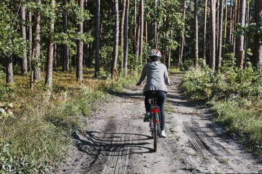 Orman yolunda bisiklet süren aktif bir kadın. Yaz tatilinde bisiklet süren bir kadın off-road rotasında. Bisiklet kaskı ve eldiven takan kadın.
