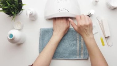 Kadın ultraviyole lamba kullanarak jel cilası sürüyor. Güzellik sağlık spa tedavisi konsepti. Kozmetik ürünler, ultraviyole lamba, beyaz masada yeşil yapraklar. Spa, manikür, cilt bakımı konsepti. Düz uzan, yukarıdan bak.