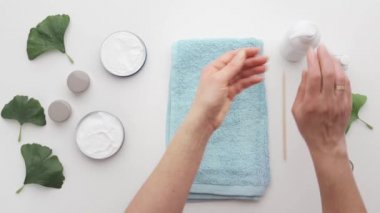 Kozmetik nemlendirici el kremi süren bir kadın. Kozmetik ürünler, beyaz masada yeşil yapraklar. Spa, manikür, cilt bakımı konsepti. Düz uzan, yukarıdan bak.