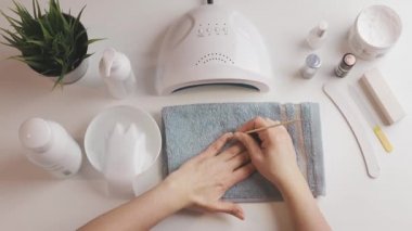Kadın, ultraviyole lamba kullanarak jel cilası sürmeye hazırlanıyor. Güzellik sağlık spa tedavisi konsepti. Kozmetik ürünler, ultraviyole lamba, beyaz masada yeşil yapraklar. Spa, manikür, cilt bakımı konsepti. Düz uzan, yukarıdan bak.