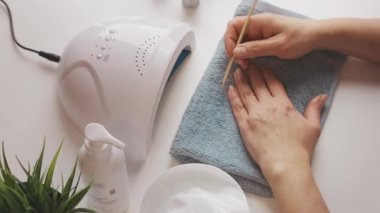 Kadın, ultraviyole lamba kullanarak jel cilası sürmeye hazırlanıyor. Güzellik sağlık spa tedavisi konsepti. Kozmetik ürünler, ultraviyole lamba, beyaz masada yeşil yapraklar. Spa, manikür, cilt bakımı konsepti. Düz uzan, yukarıdan bak.