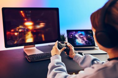 Evde video oyunu oynayan ergen kız. Oyuncular ekranın önünde oyun kağıtlarını tutuyorlar. Karanlık odada oynayan flamalar neon ışıklarıyla aydınlatılıyor. Rekabet ve eğlence.