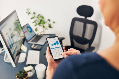 İş kadını akıllı telefon ve bilgisayardaki tablolar ve tablolar üzerinde finansal verilerle çalışıyor. Satış istatistiklerine bakan kadın girişimci ofiste masanın başında duruyor.