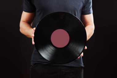 Plak kaydı olan bir adam. Klasik müzik tarzı. Siyah arka planda duran mavi tişörtlü bir erkek eski müzik rekorunu elinde tutuyor. Retro müzik. Klasik ses.