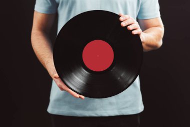 Plak kaydı olan bir adam. Klasik müzik tarzı. Siyah arka planda duran siyah analog disk tutan mavi tişörtlü bir erkek. Retro müzik. Klasik ses.