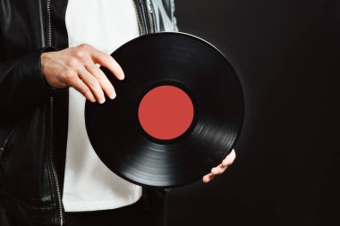 Plak kaydı olan bir adam. Klasik müzik tarzı. Rock tarzı. Siyah ceketli bir erkek, pikabını siyah arka planda tutuyor. Retro müzik. Klasik ses kaydı. Uzayı sağa kopyala