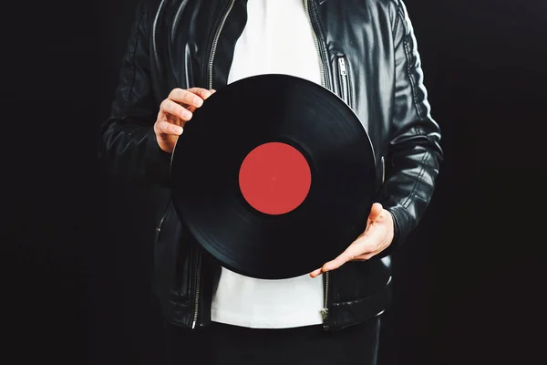 Man holding vinyl record. Vintage music style. Rock Style. Male wearing black jacket holding black disc standing on dark background. Retro music. Classic audio