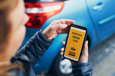 Akıllı telefondan mobil park uygulaması kullanan bir kadın. Şoför park ücretini ödemek için akıllı telefonu kullanıyor. Cep telefonundan otopark başvurusu. Çevrimiçi hızlı ödemeyle park ücretini ödemeye elverişli. Mobil park servisi