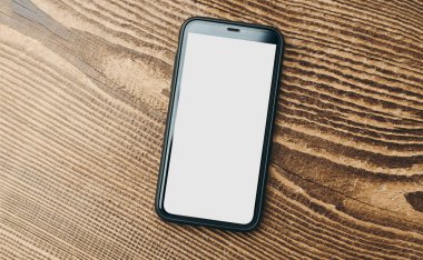 Ahşap zemin üzerinde beyaz, boş ve izole bir ekran olan akıllı telefon modeli. Siyah cep telefonu üst görünümü düz ve fotokopi alanı var. İçerik için hazır. Metin için yer