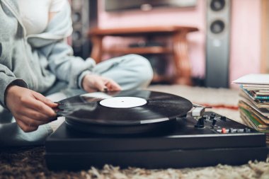 Young woman listening to music from vinyl record player. Retro and vintage music style. Girl holding analog record album sitting in room at home. Female enjoying music from old record collection