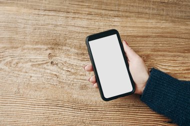 Beyaz, boş, ahşap arka planda boş ekranı olan akıllı telefon modeli tutan bir kadın. Teknolojiyi kullanan kişi. Kopya alanı kalan cep telefonu. İçerik için hazır. Metin için yer