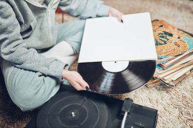 Vinil pikaptan müzik dinleyen genç bir kadın. Retro ve klasik müzik tarzı. Analog albüm tutan kız evde oturuyor. Eski plak koleksiyonundan müziğin keyfini çıkaran bir kadın