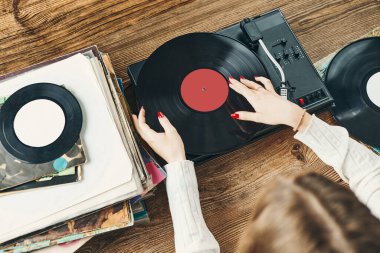 Vinil pikaptan müzik dinleyen genç bir kadın. Pikapta müzik çalıyor. Kadın, evdeki eski plak koleksiyonundan müziğin keyfini çıkarıyor. Analog vinil plak yığını. Retro ve klasik müzik tarzı. Müzik tutkusu ve hobisi
