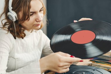 Vinil pikaptan müzik dinleyen genç bir kadın. Pikapta müzik çalıyor. Kadın, evdeki eski plak koleksiyonundan müziğin keyfini çıkarıyor. Analog vinil plak yığını. Retro ve klasik müzik tarzı. Müzik tutkusu ve hobisi