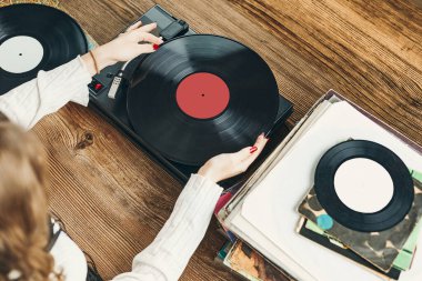 Vinil pikaptan müzik dinleyen genç bir kadın. Pikapta müzik çalıyor. Kadın, evdeki eski plak koleksiyonundan müziğin keyfini çıkarıyor. Analog vinil plak yığını. Retro ve klasik müzik tarzı. Müzik tutkusu ve hobisi