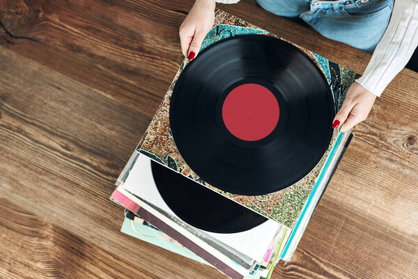 Playing vinyl records. Listening to music from vinyl record player. Retro and vintage music style. Woman holding analog LP record album. Stack of old records. Music collection. Music passion