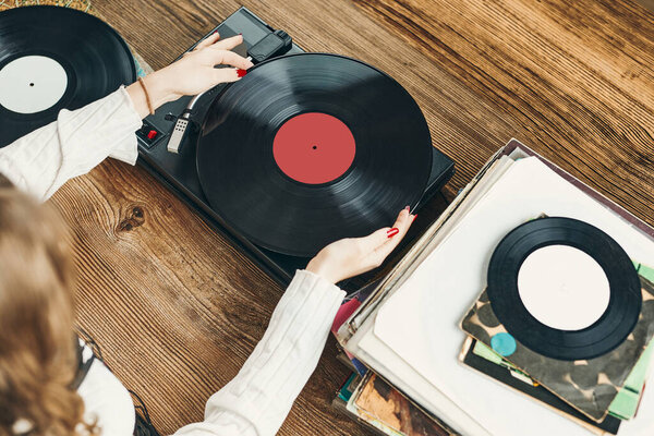 Young woman listening to music from vinyl record player. Playing music on turntable player. Female enjoying music from old record collection at home. Stack of analog vinyl records. Retro and vintage music style. Music Passion and hobby