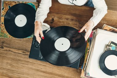 Vinil pikaptan müzik dinleyen genç bir kadın. Pikapta müzik çalıyor. Kadın, evdeki eski plak koleksiyonundan müziğin keyfini çıkarıyor. Analog vinil plak yığını. Retro ve klasik müzik tarzı. Müzik tutkusu ve hobisi