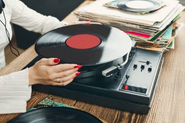 Vinil pikaptan müzik dinleyen genç bir kadın. Pikapta müzik çalıyor. Kadın, evdeki eski plak koleksiyonundan müziğin keyfini çıkarıyor. Analog vinil plak yığını. Retro ve klasik müzik tarzı. Müzik tutkusu ve hobisi