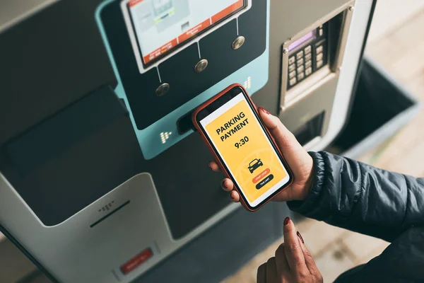 Woman paying for parking ticket at car parking payment machine using mobile app on smartphone. Driver using smartphone to pay for parking. Car park application on mobile phone. Convienience paying for parking using fast payment online. Mobile park se