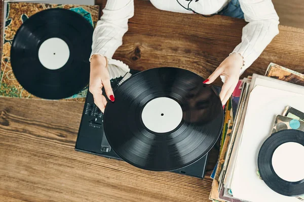 Young woman listening to music from vinyl record player. Playing music on turntable player. Female enjoying music from old record collection at home. Stack of analog vinyl records. Retro and vintage music style. Music Passion and hobby