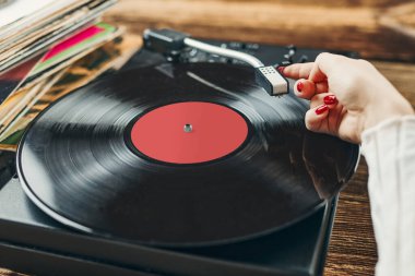 Vinil pikaptan müzik dinleyen genç bir kadın. Pikapta müzik çalıyor. Kadın, evdeki eski plak koleksiyonundan müziğin keyfini çıkarıyor. Analog vinil plak yığını. Retro ve klasik müzik tarzı. Müzik tutkusu ve hobisi