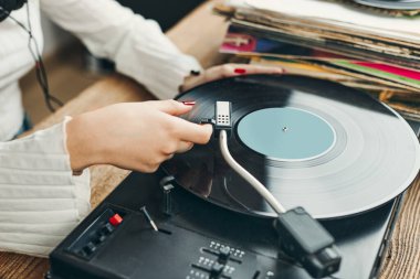 Vinil pikaptan müzik dinleyen genç bir kadın. Pikapta müzik çalıyor. Kadın, evdeki eski plak koleksiyonundan müziğin keyfini çıkarıyor. Analog vinil plak yığını. Retro ve klasik müzik tarzı. Müzik tutkusu ve hobisi