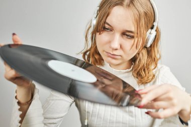 Vinil pikaptan müzik dinleyen genç bir kadın. Pikapta müzik çalıyor. Kadın, evdeki eski plak koleksiyonundan müziğin keyfini çıkarıyor. Analog vinil plak yığını. Retro ve klasik müzik tarzı. Müzik tutkusu ve hobisi