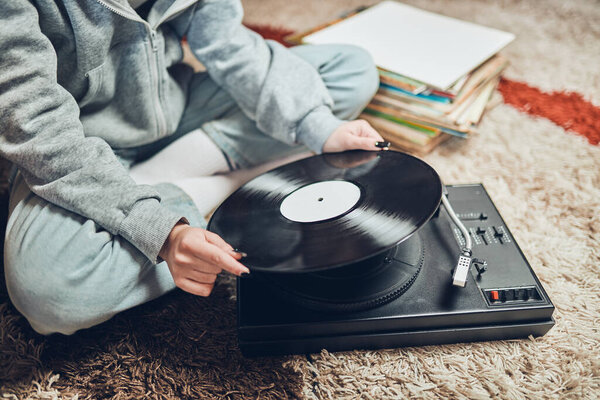Young woman listening to music from vinyl record player. Retro and vintage music style. Girl holding analog record album sitting in room at home. Female enjoying music from old record collection