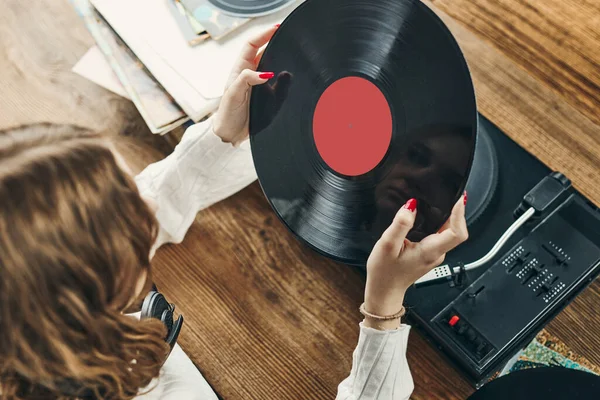 Young woman listening to music from vinyl record player. Playing music on turntable player. Female enjoying music from old record collection at home. Stack of analog vinyl records. Retro and vintage music style. Music Passion and hobby
