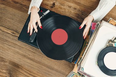 Vinil pikaptan müzik dinleyen genç bir kadın. Pikapta müzik çalıyor. Kadın, evdeki eski plak koleksiyonundan müziğin keyfini çıkarıyor. Analog vinil plak yığını. Retro ve klasik müzik tarzı. Müzik tutkusu ve hobisi