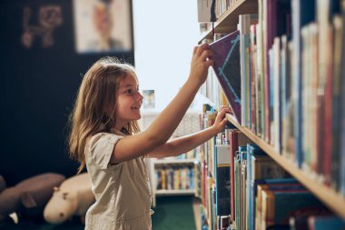 Okul kütüphanesinde kitap seçen liseli kız. Okumak için edebiyat seçen zeki bir kız. Kitapçıdaki raflardaki kitaplar. Kitaplardan öğreniyorum. Okul eğitimi. Günlük okumanın faydaları. Çocuk merakı. Okula geri dön.