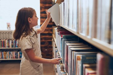 Okul kütüphanesinde kitap seçen liseli kız. Kitap seçen akıllı kız. Kitapçıdaki raflardaki kitaplar. Kitaplardan öğreniyorum. Okul eğitimi. Günlük okumanın faydaları. Çocuk merakı. Okula geri dön.