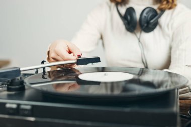 Vinil pikaptan müzik dinleyen genç bir kadın. Pikapta müzik çalıyor. Kadın, evdeki eski plak koleksiyonundan müziğin keyfini çıkarıyor. Analog vinil plak yığını. Retro ve klasik müzik tarzı. Müzik tutkusu ve hobisi