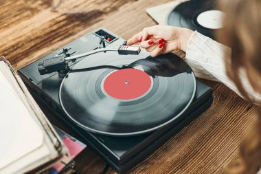 Vinil pikaptan müzik dinleyen genç bir kadın. Pikapta müzik çalıyor. Kadın, evdeki eski plak koleksiyonundan müziğin keyfini çıkarıyor. Analog vinil plak yığını. Retro ve klasik müzik tarzı. Müzik tutkusu ve hobisi