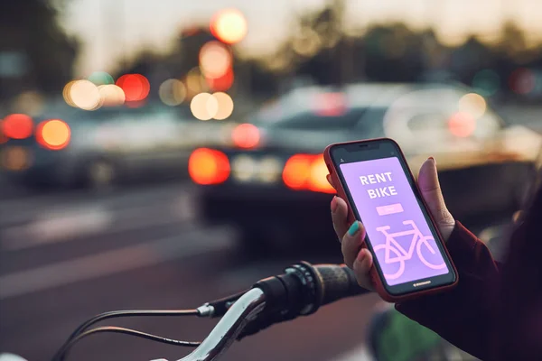 Woman renting bike using rental app on mobile phone. Using bike sharing city service. Paid rent of electric scooter. Using smartphone to rent and pay for public eco transport. Female holding smart phone standing at bike sharing city station. Ecologic