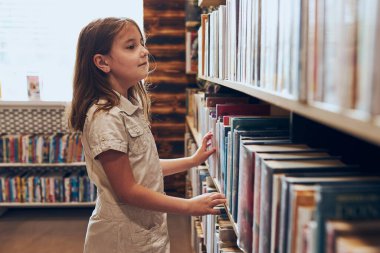 Okul kütüphanesinde kitap seçen liseli kız. Kitap seçen akıllı kız. Kitapçıdaki raflardaki kitaplar. Kitaplardan öğreniyorum. Okul eğitimi. Günlük okumanın faydaları. Çocuk merakı. Okula geri dön.