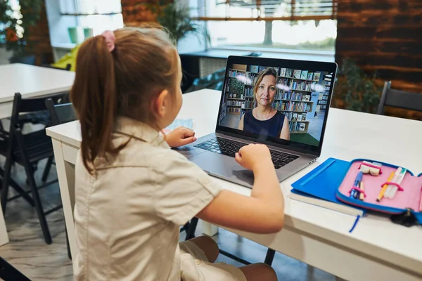 Student litttle girl having video class remotely with her teacher on laptop sitting at desk in after school club at primary school. Back to school. Child using technology on elementary computer science lesson. Smart little girl learning online. Teach